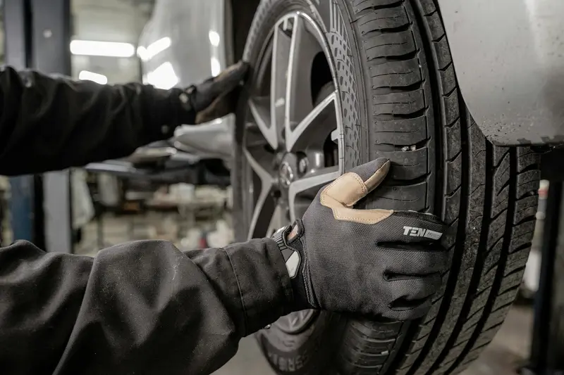 Tyre fitter in work gloves fitting a wheel to a car